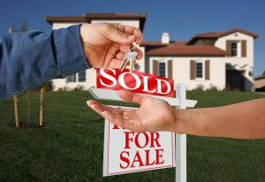 Person receiving the keys to a home, in front of a SOLD real estate sign