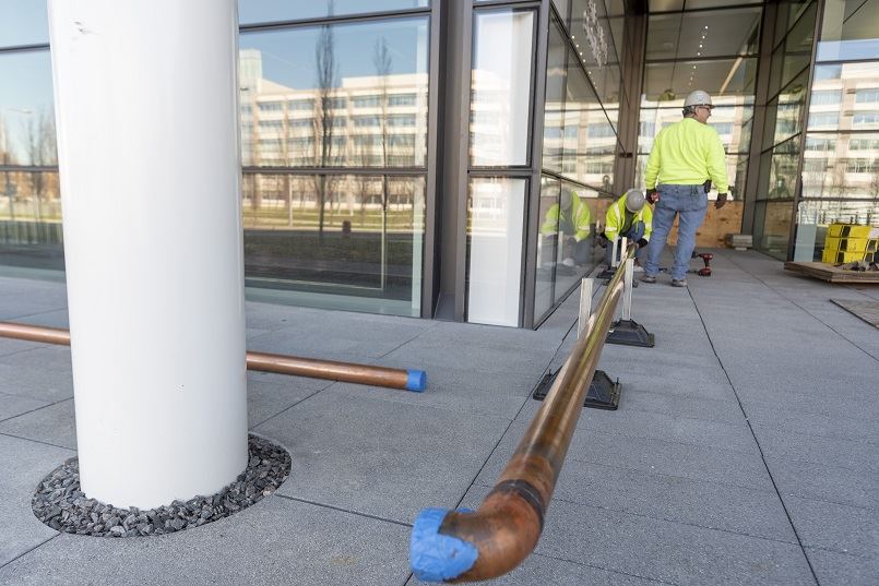 Pipefitters working on a new copper pipe outside an office building